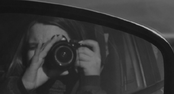 Valentina photographed through a car side mirror, holding a camera